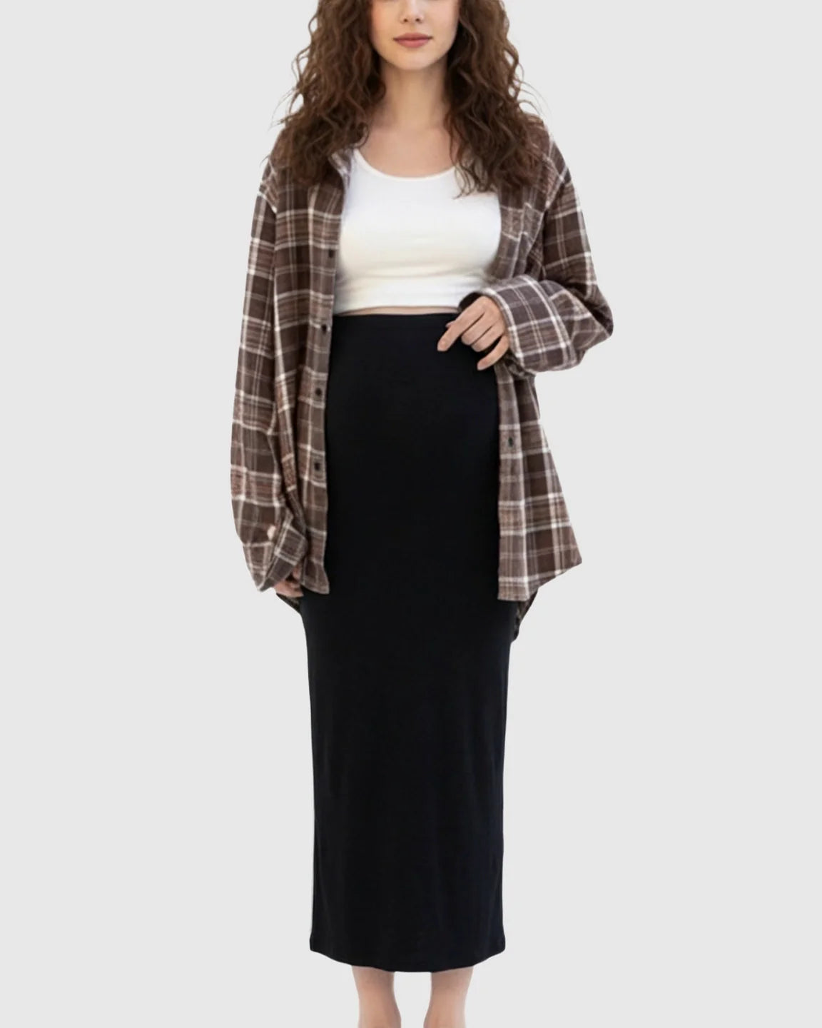 Woman wearing a black, skin-friendly maternity midi skirt with a white top and brown plaid shirt.