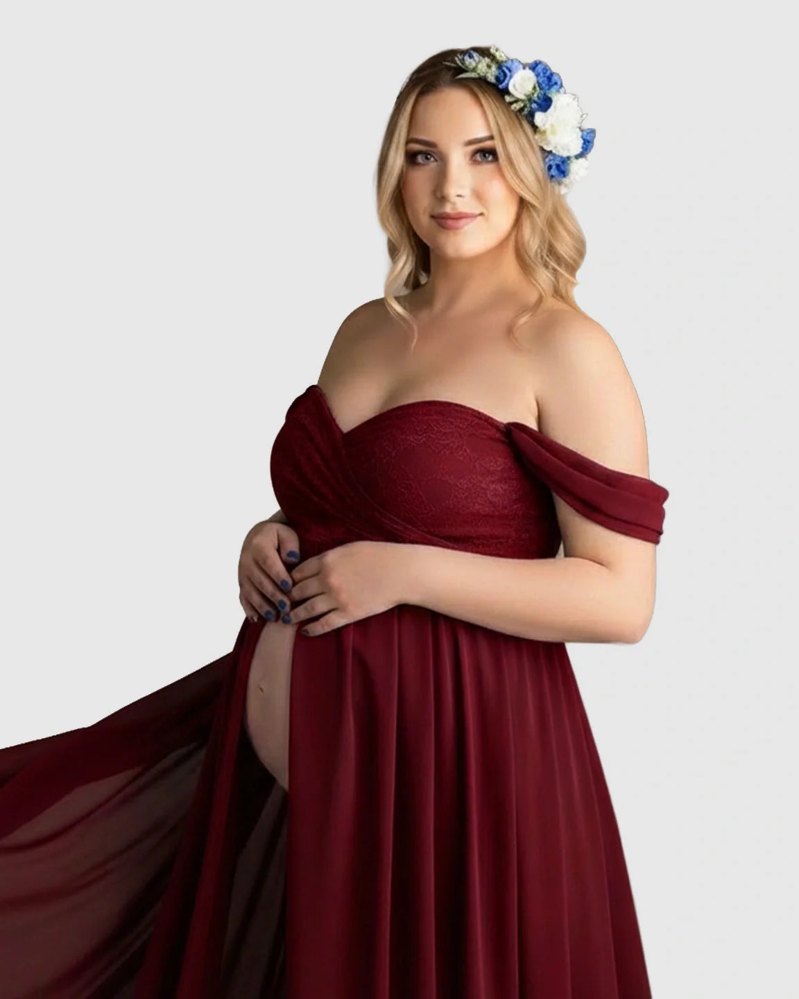 Pregnant woman in a red off-shoulder chiffon maternity gown with a long train and floral headpiece.