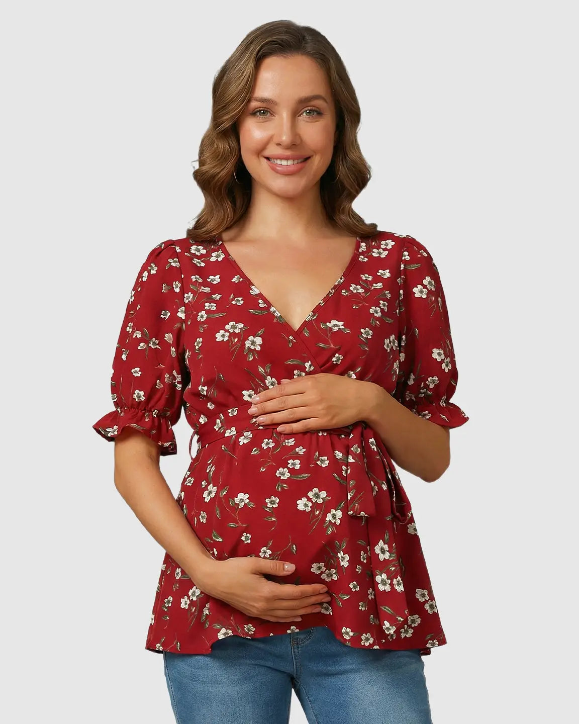 Smiling pregnant woman in a red floral crossover V-neck maternity and nursing top with puff sleeves and tie waist.