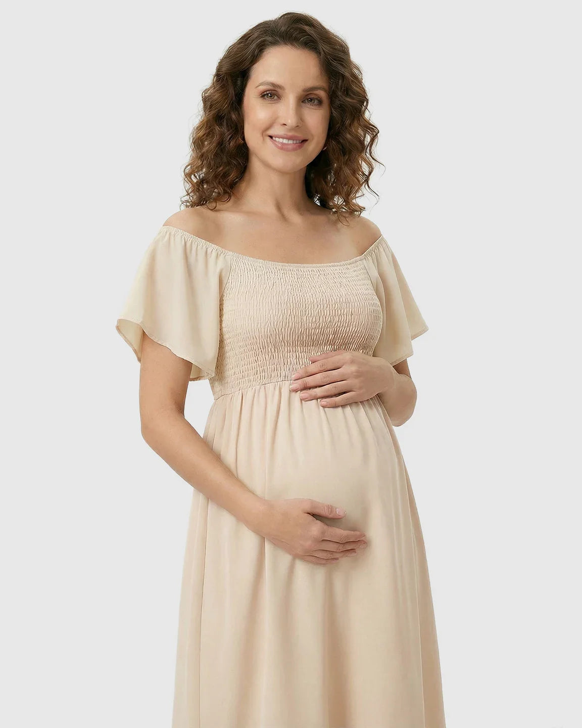 Smiling pregnant woman in a beige flutter-sleeve smocked maternity midi dress.
