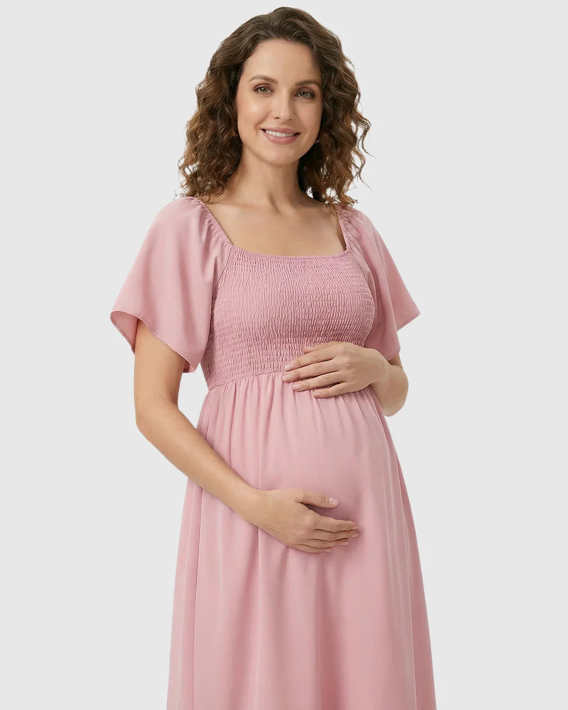 Smiling pregnant woman in a pink flutter-sleeve smocked maternity midi dress.