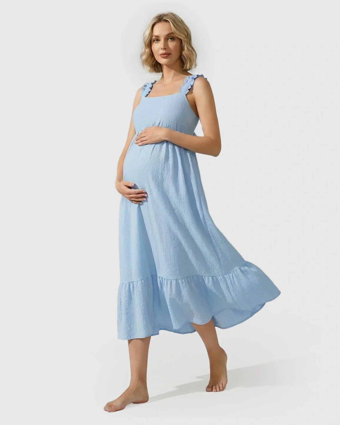 Pregnant woman in a light blue ruffled strap tiered maternity maxi dress, holding her bump.