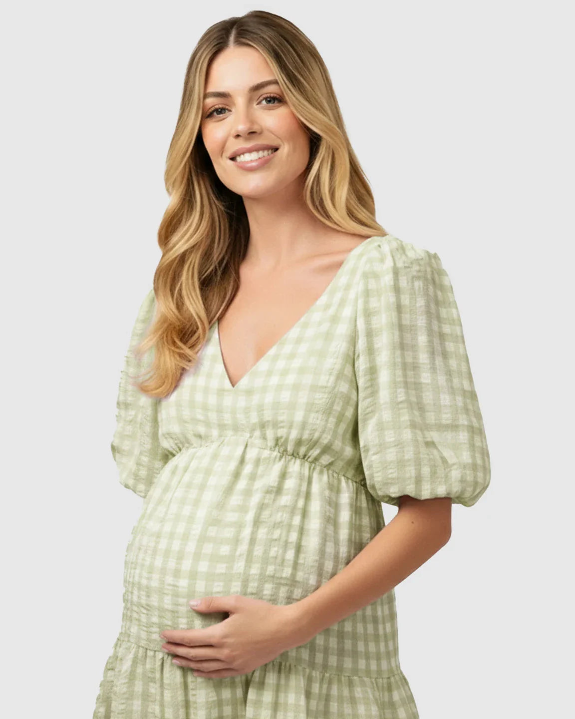 Smiling pregnant woman in a green and white checkered maternity maxi dress with puffed sleeves.