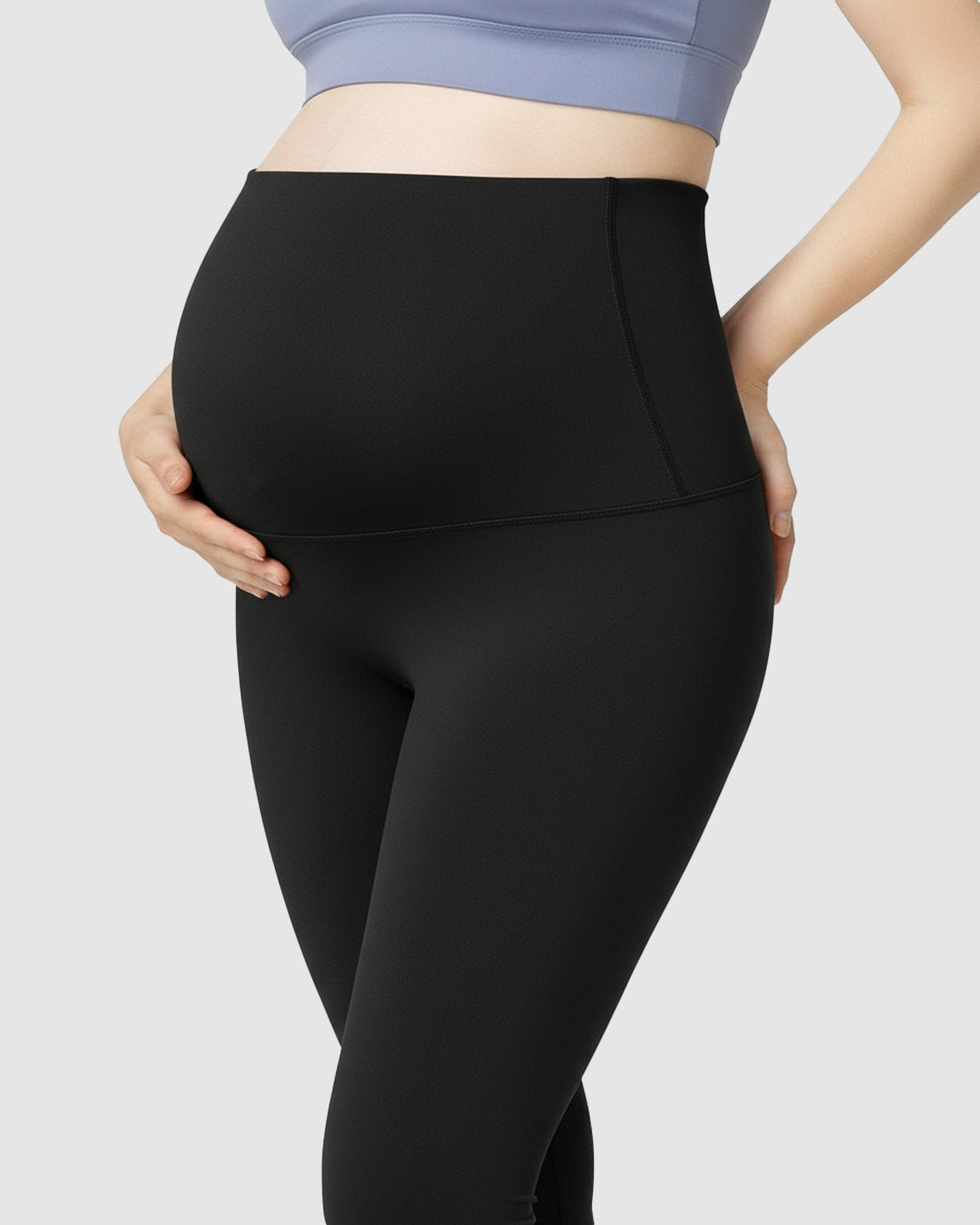 Pregnant woman wearing black high-waist soft stretch maternity leggings, supporting her bump.