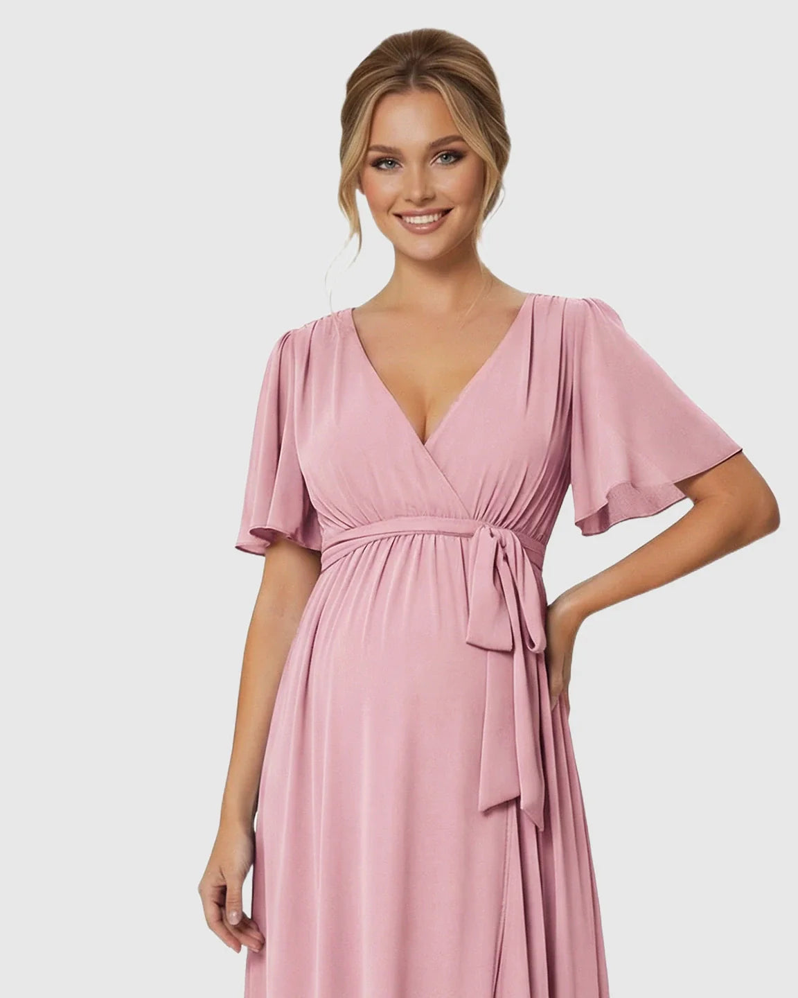 Smiling pregnant woman in a pink surplice V-neck flutter sleeve maternity maxi dress with a front slit and empire waist tie.