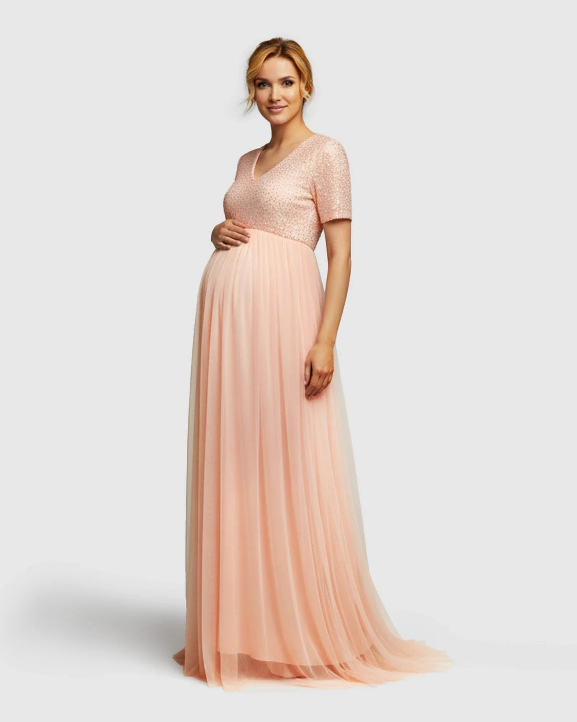 Smiling pregnant woman in a pink sequin A-line maternity evening gown with a flowing train.