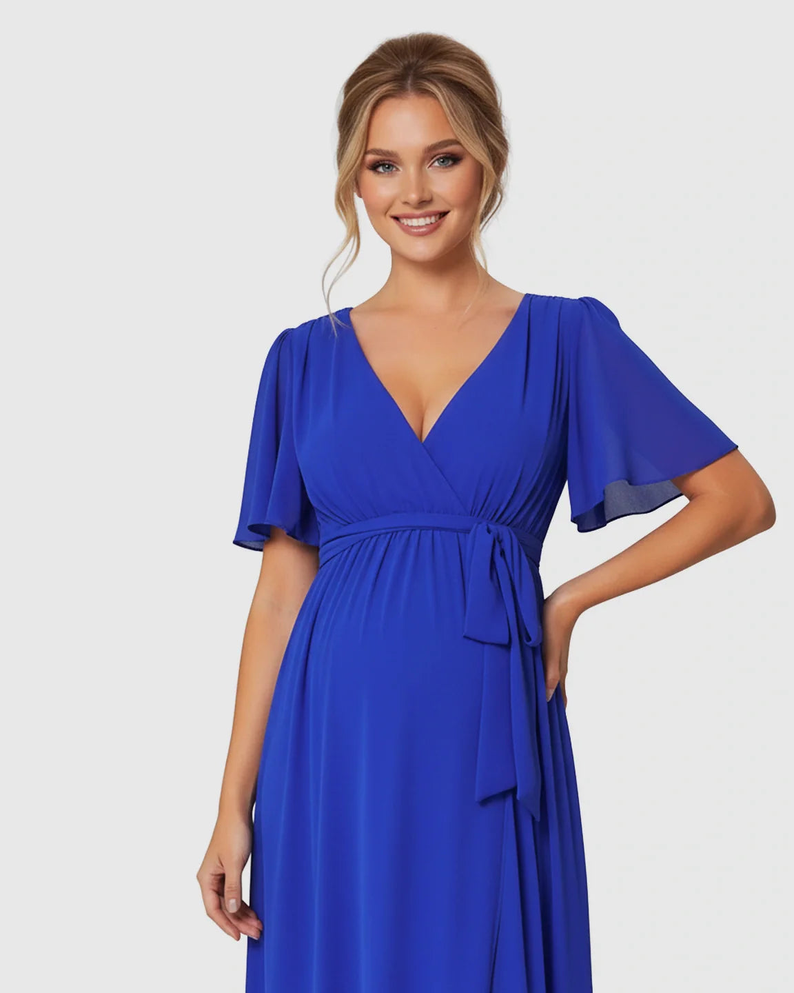 Smiling pregnant woman in a royal blue surplice V-neck flutter sleeve maternity maxi dress with a front slit.
