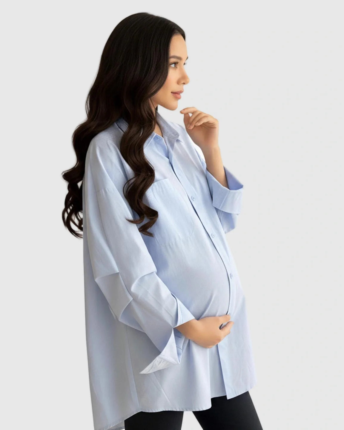 Pregnant woman in a light blue cotton lapel-collar button-front maternity tunic, holding her bump.