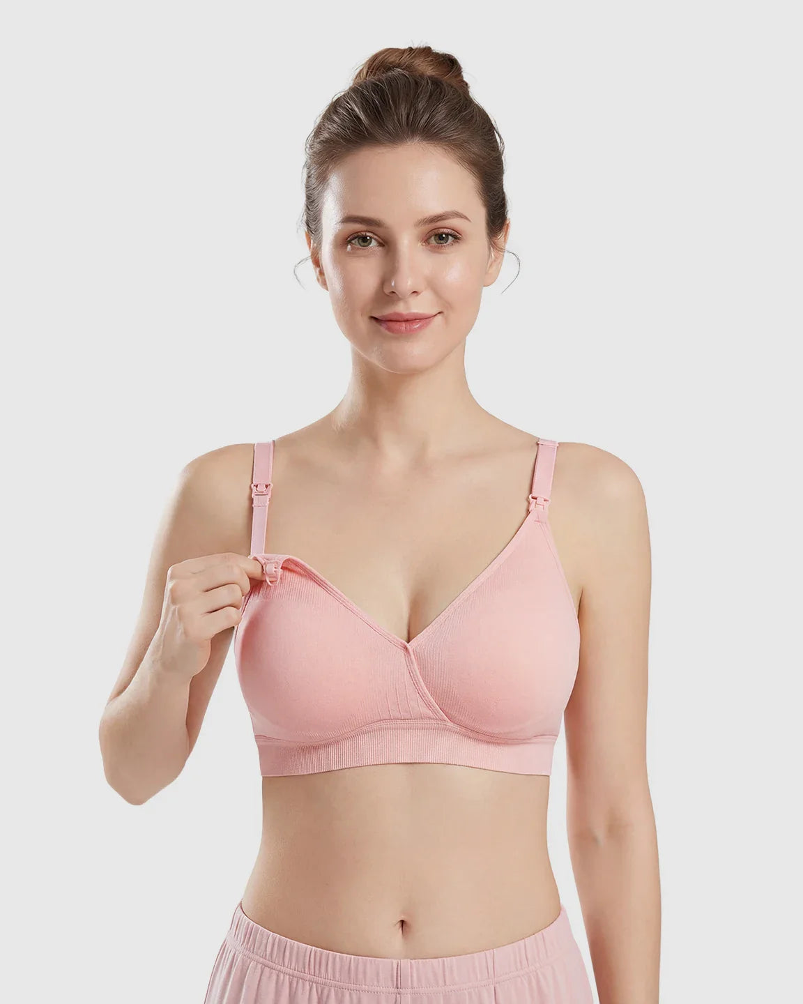 Woman models a pink seamless cross-front wireless nursing bra, demonstrating the easy-access clip.