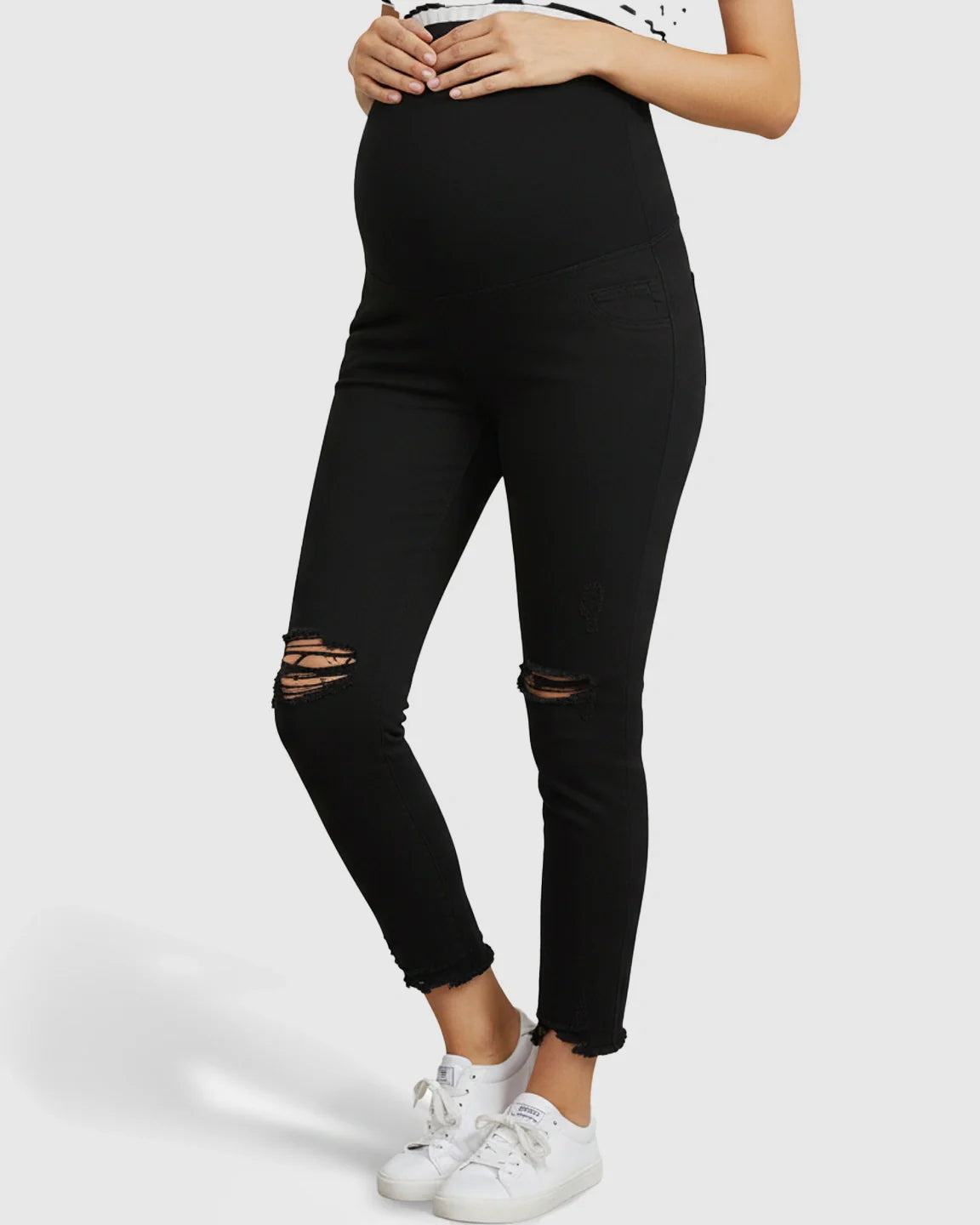Black maternity skinny jeans with over-belly support panel, distressed knees, and ankle-fray hem.