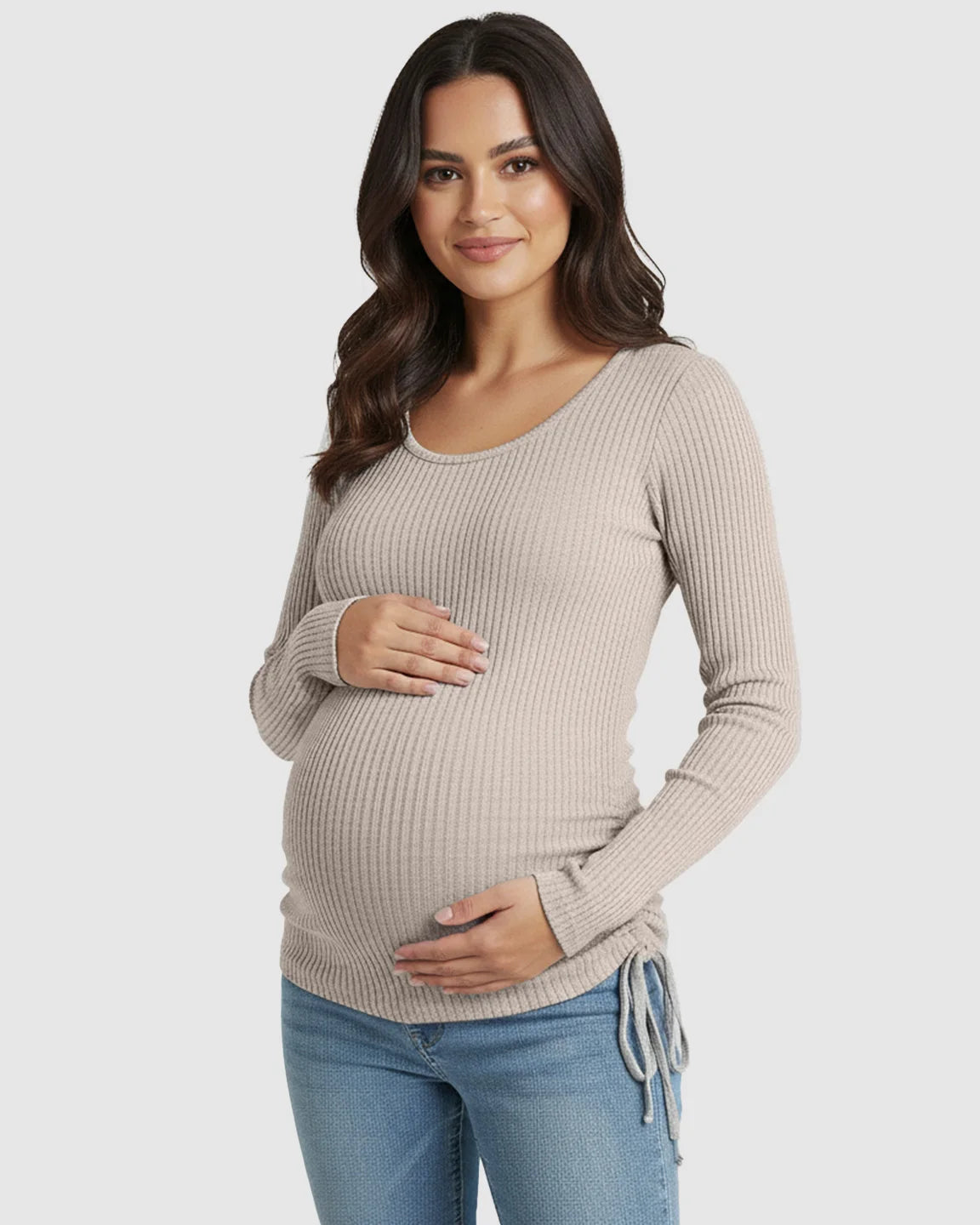 Pregnant woman in a beige ribbed long-sleeve maternity top with adjustable side drawstrings, paired with jeans.