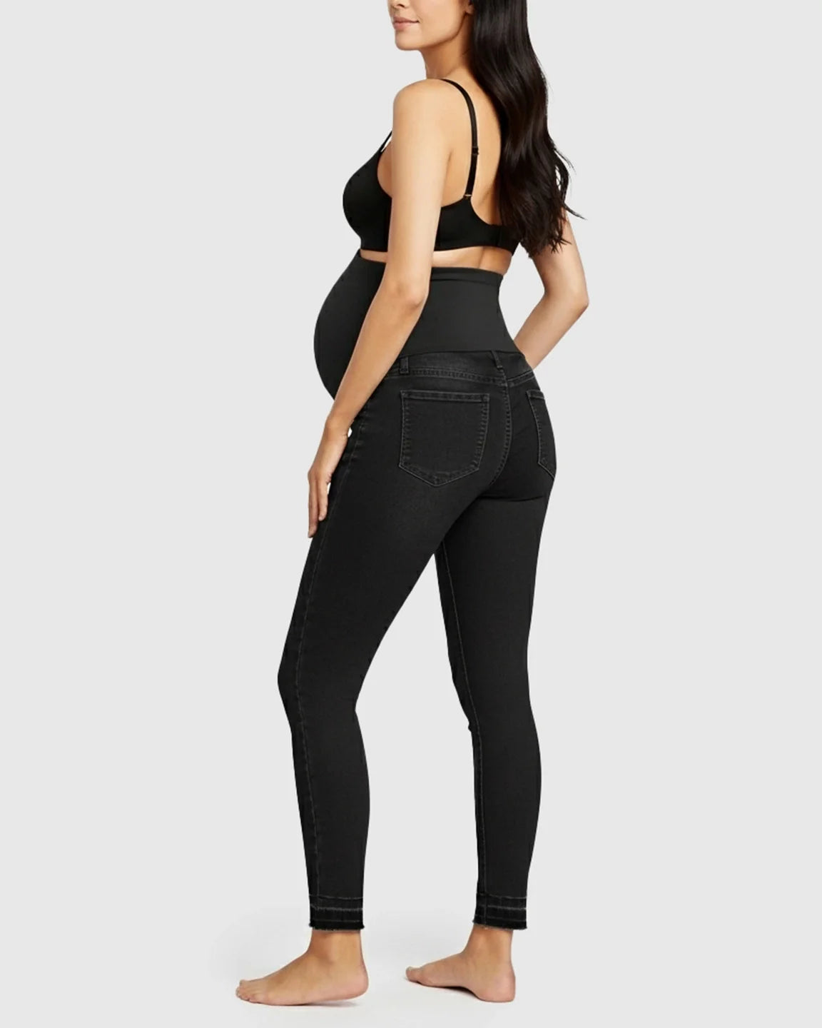 Woman in black high-waist skinny maternity jeans with an elastic waistband, seen from the back.