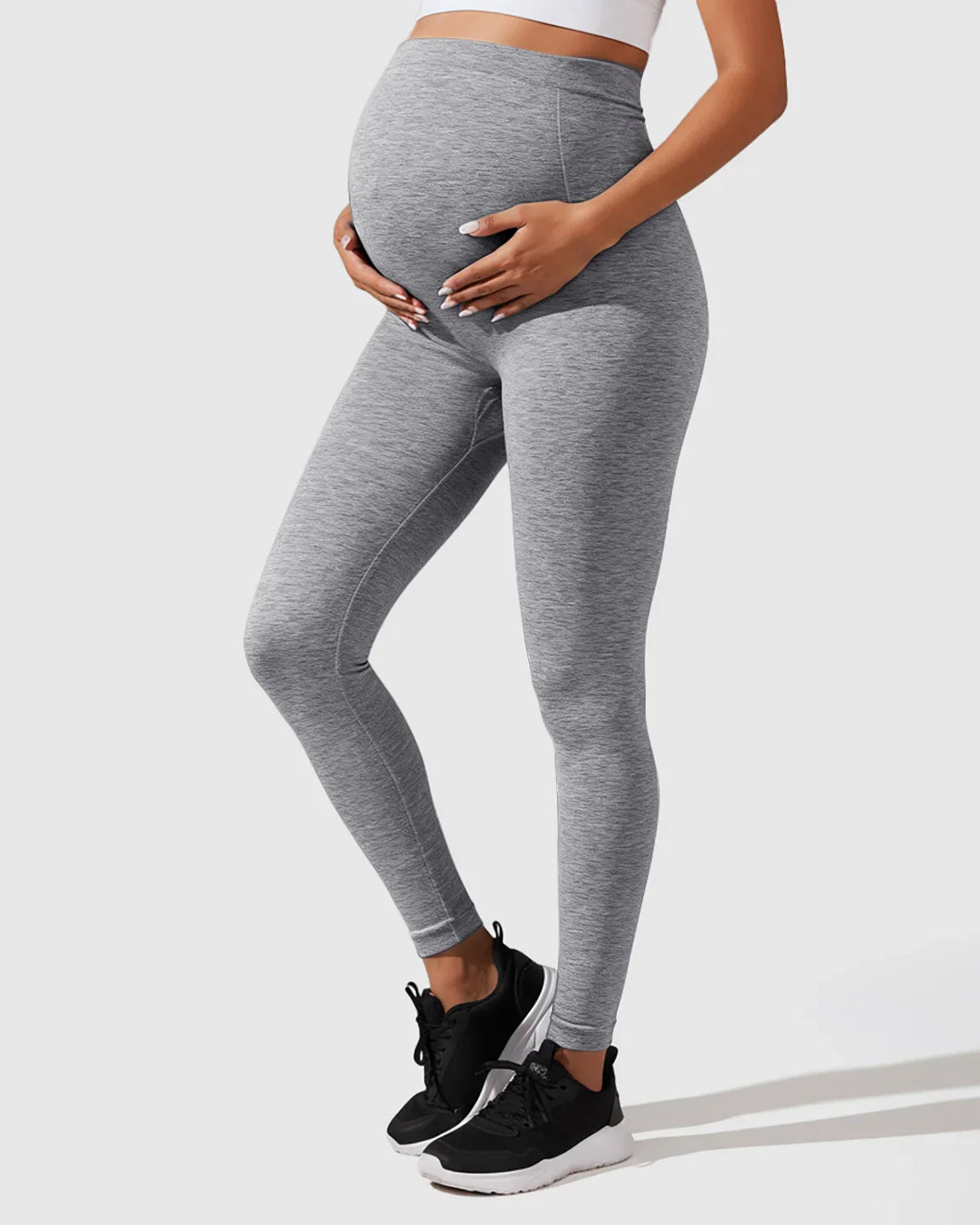 Pregnant woman wearing heather gray seamless high-waisted maternity leggings, gently cradling her bump.