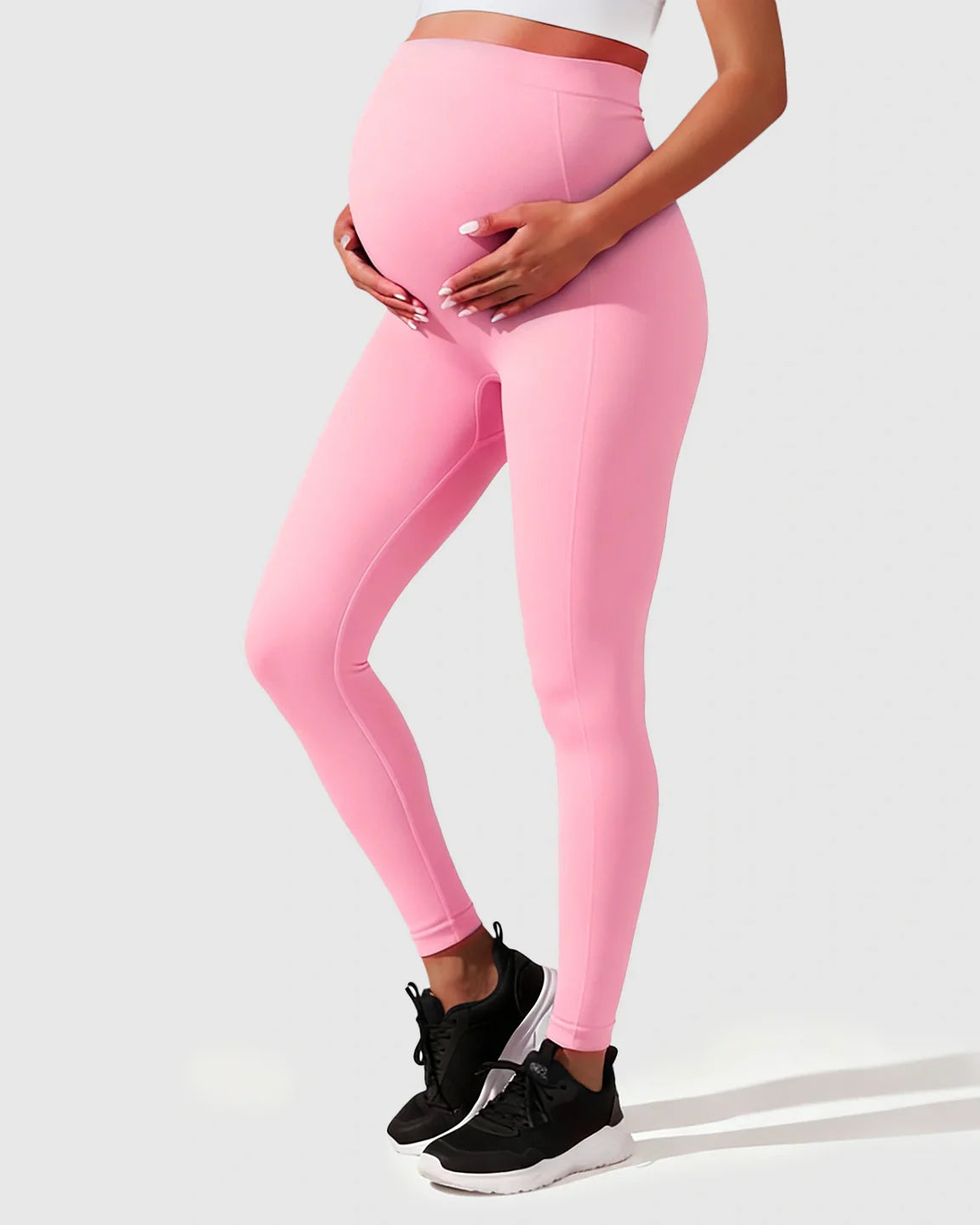 Pregnant woman wearing pink seamless high-waisted maternity leggings, gently holding her bump.