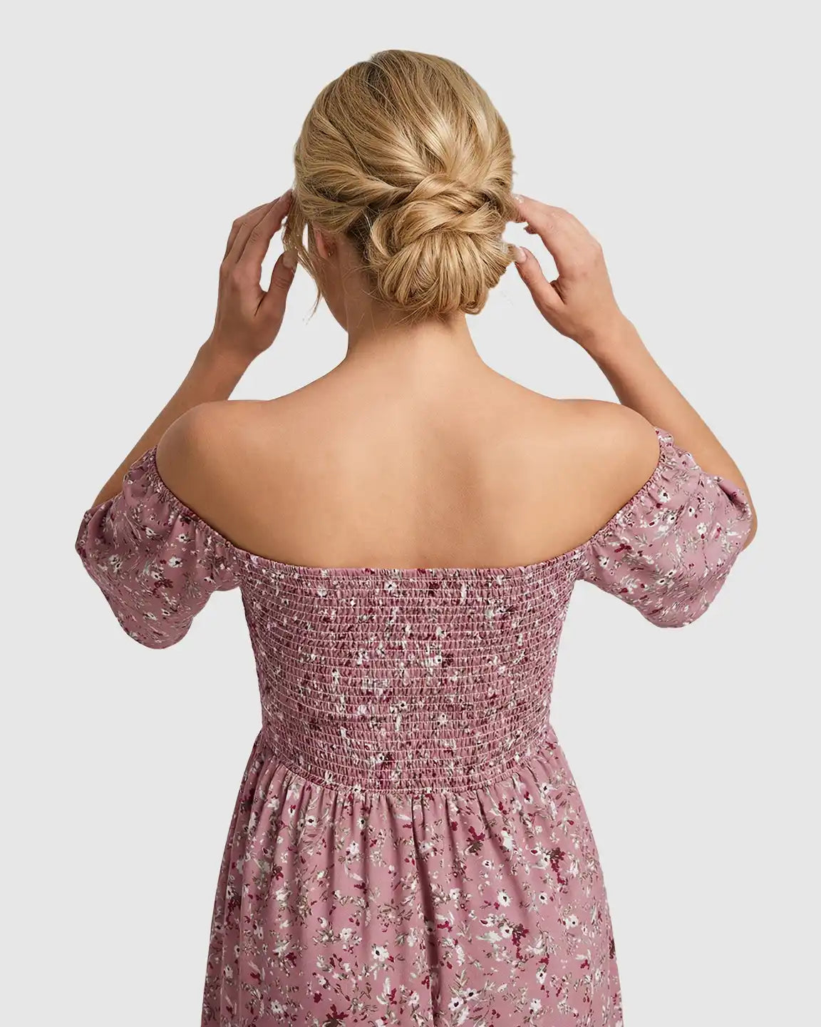 Back view of a woman wearing a pink floral flutter-sleeve smocked maternity midi dress.