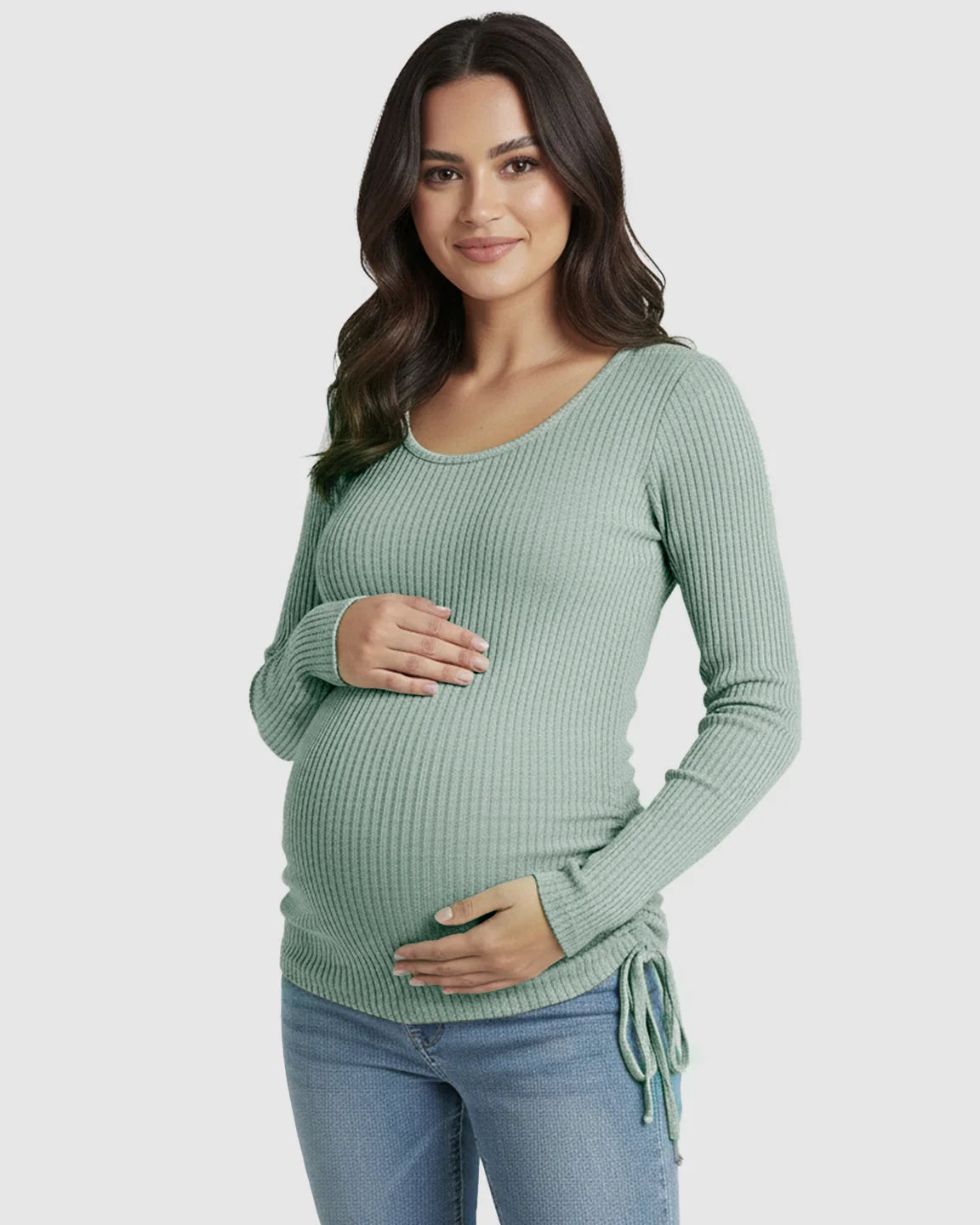Smiling pregnant woman in a sage green ribbed maternity top with adjustable side drawstrings and a U-neck.