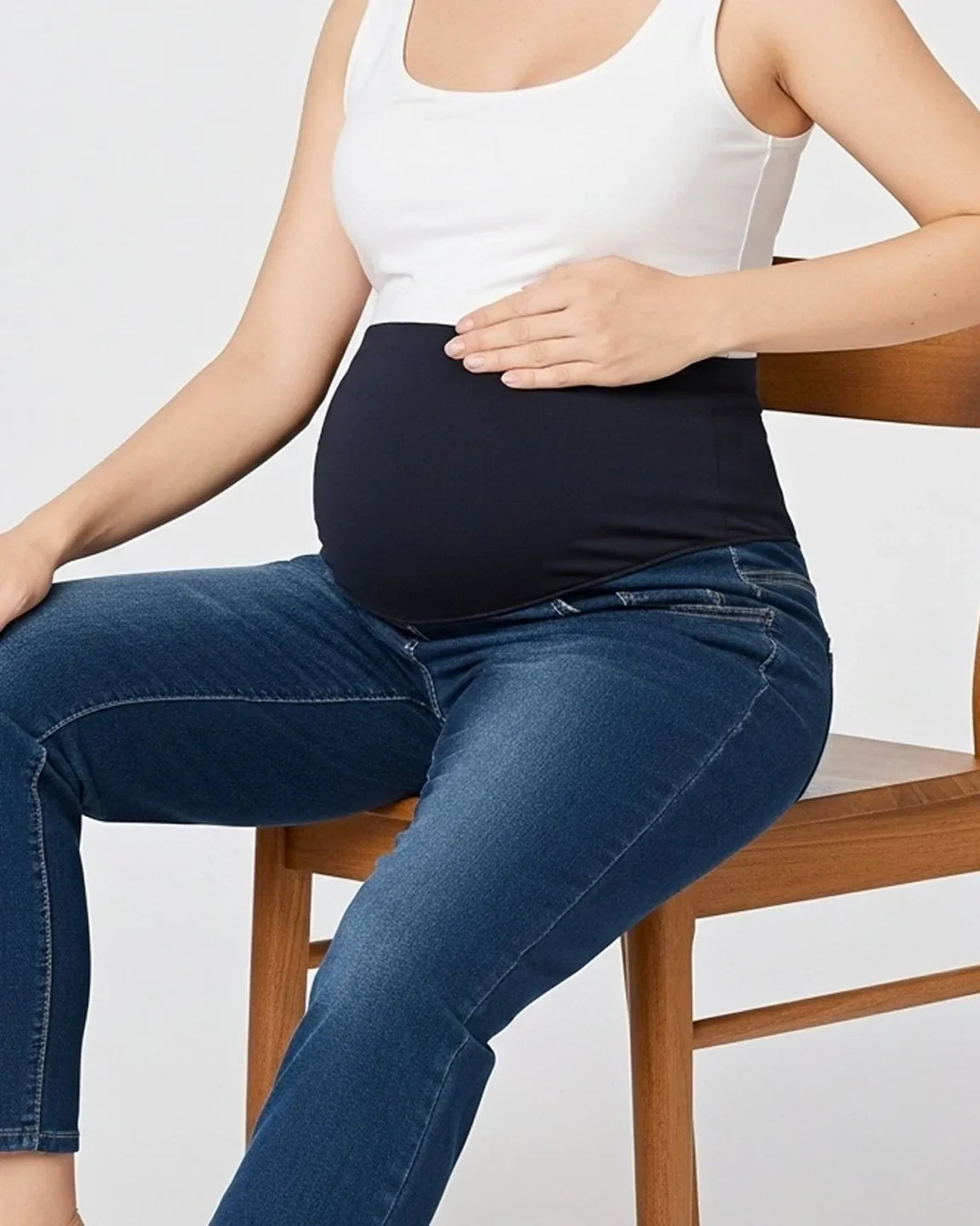 Pregnant woman in dark wash straight-leg maternity jeans with a black belly support panel and white tank top.