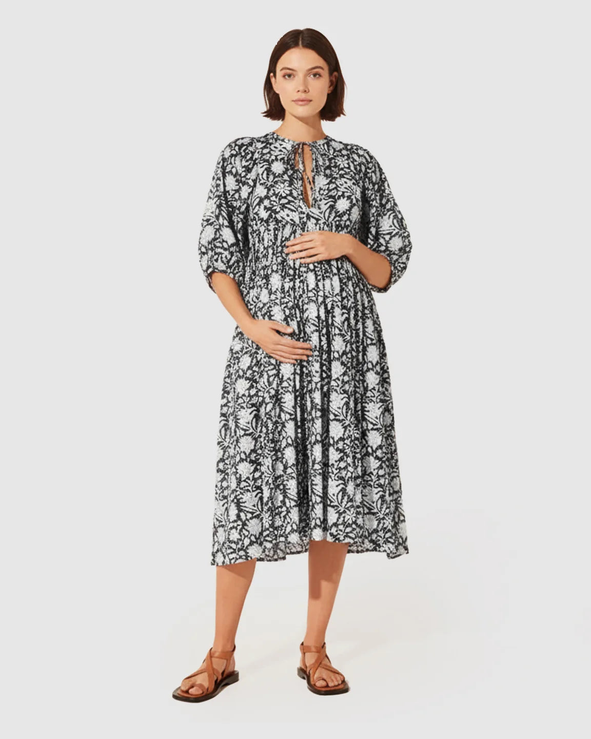 Pregnant model in a black and white floral loose fit maternity midi dress with gathered shoulders and puff sleeves.