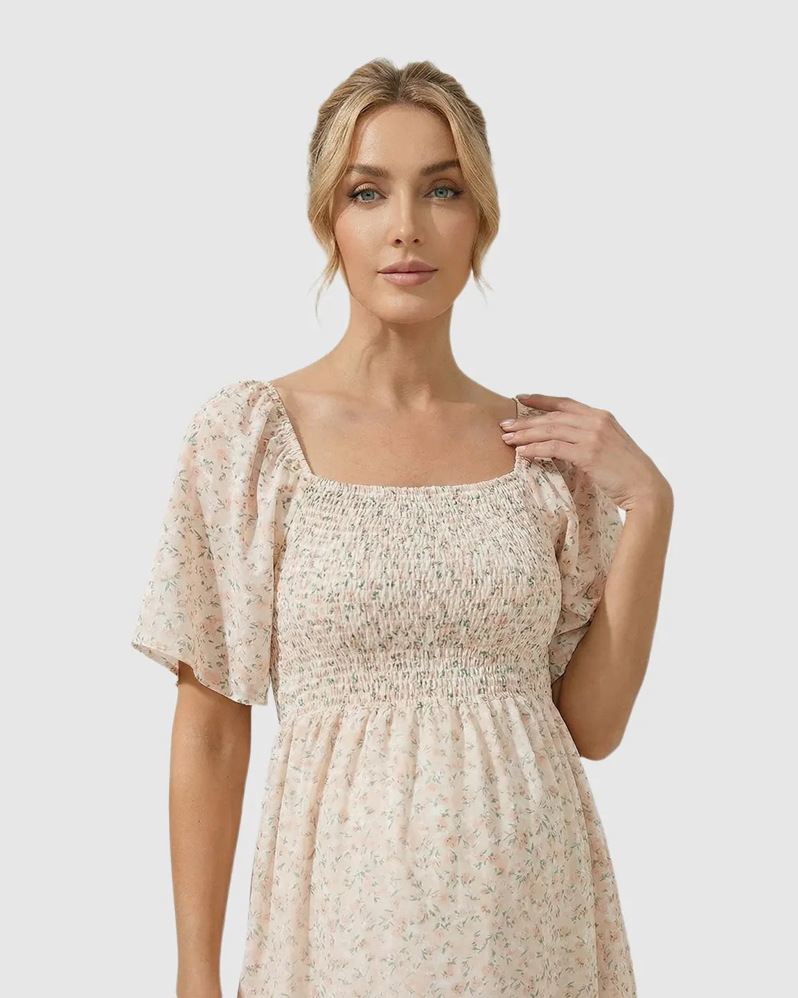 Blonde woman in a light pink floral flutter-sleeve smocked maternity midi dress, cotton-polyester blend.