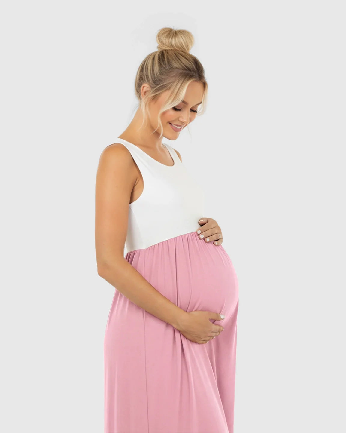 Smiling pregnant woman in a white and pink colorblock high-waisted maternity maxi dress, holding her bump.