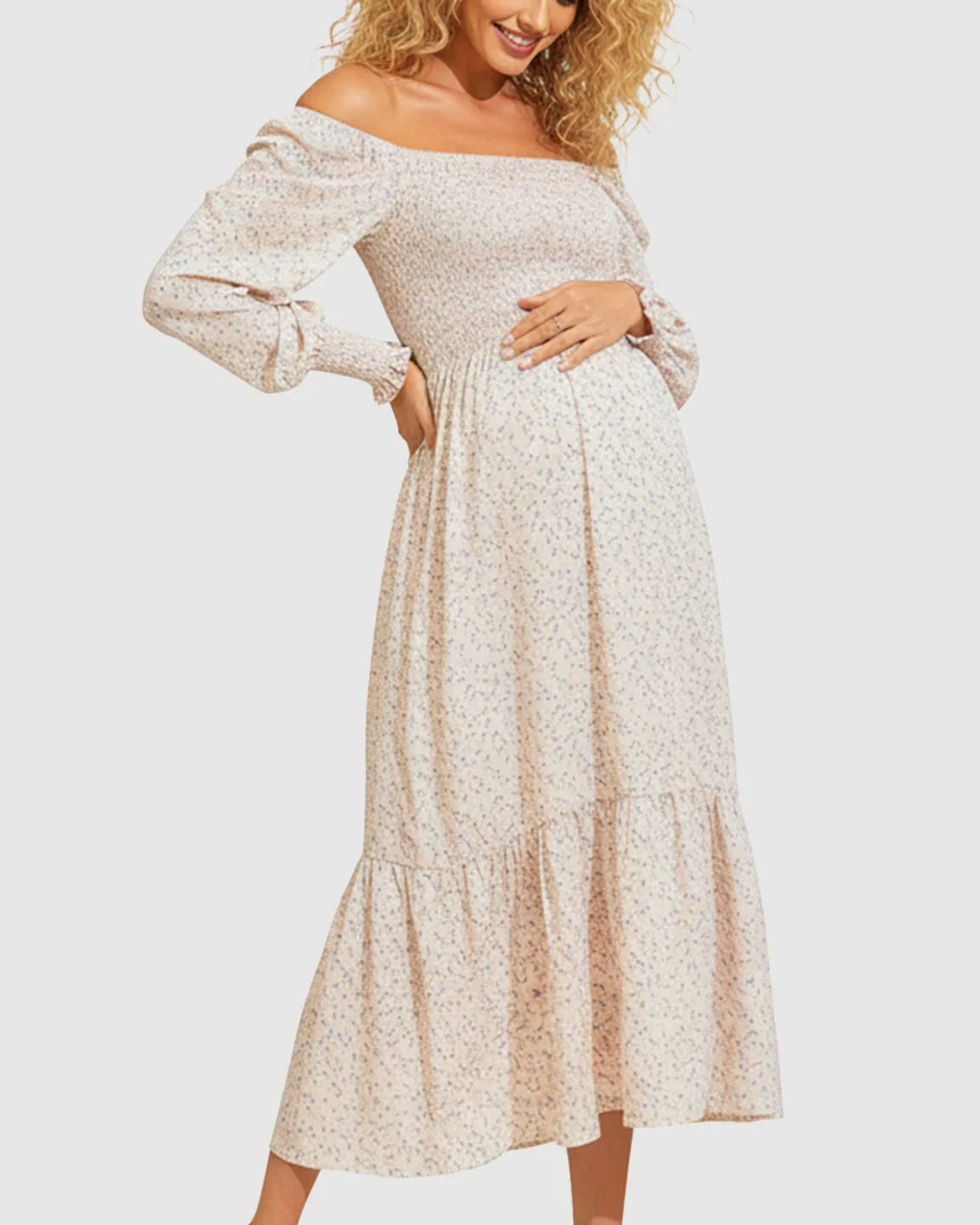 Off-shoulder flowy maternity midi dress in light pink with blue floral print, smocked bodice, and tiered skirt.