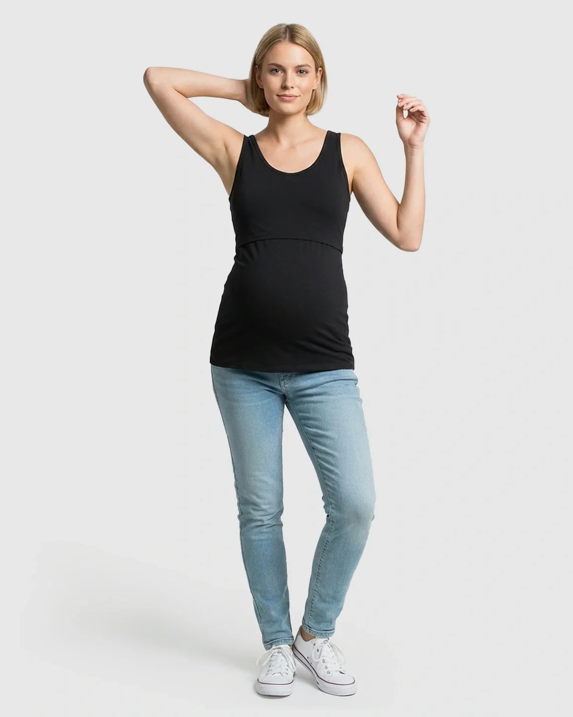 Woman in black stretch nursing-access maternity tank top, light wash jeans, and white sneakers.
