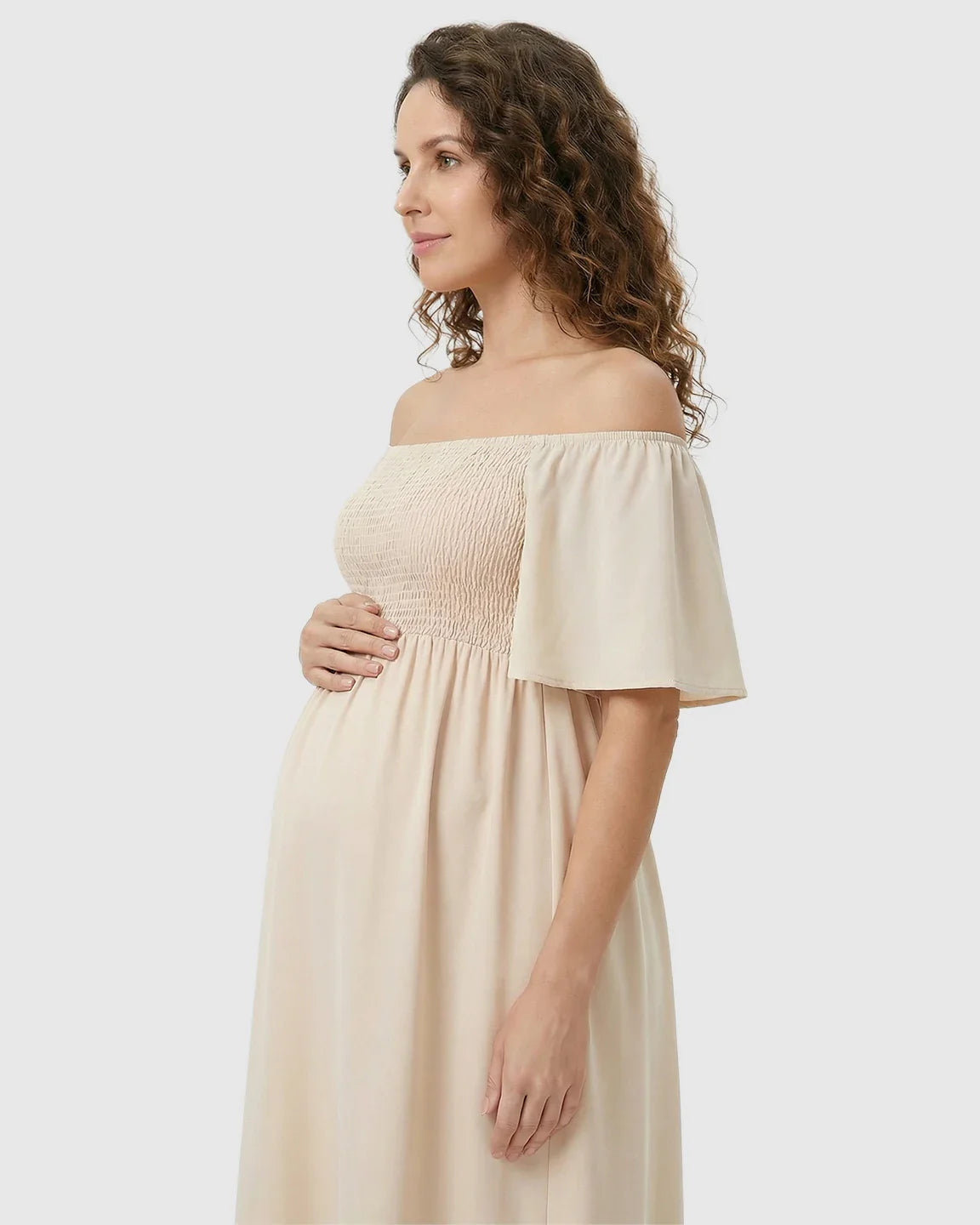 Pregnant woman in a beige off-shoulder smocked maternity midi dress with flutter sleeves.