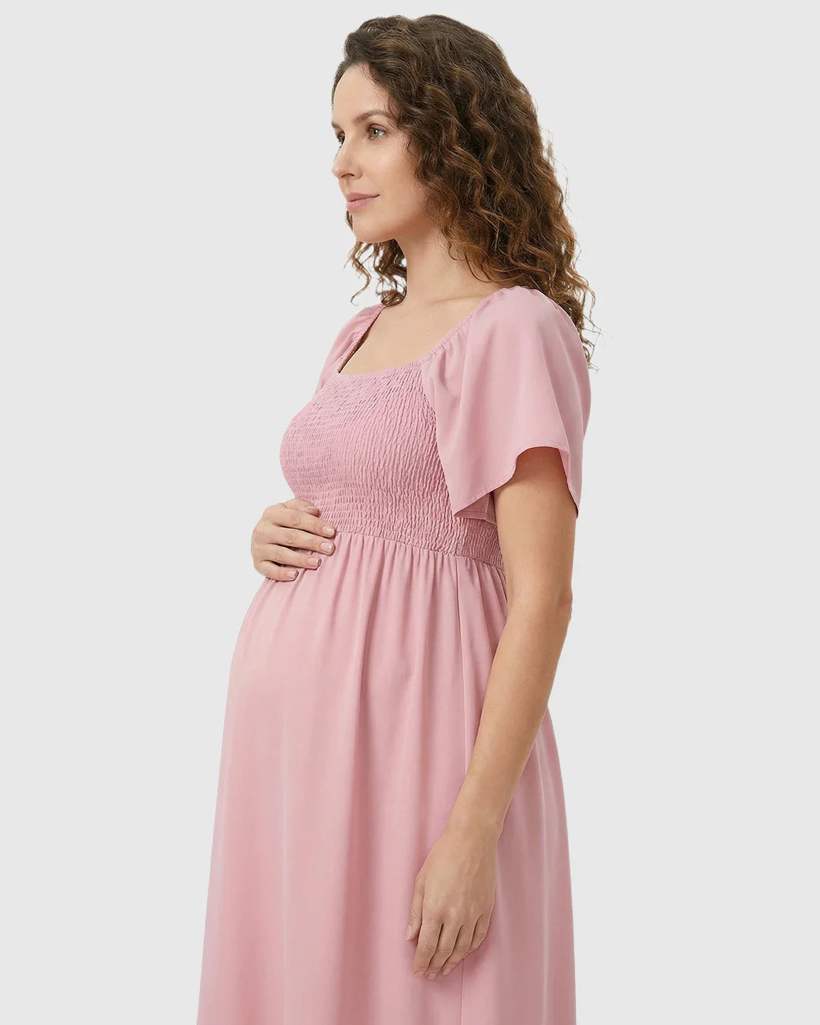 Pink flutter-sleeve smocked maternity midi dress with a tiered flowy skirt, worn by a pregnant woman.