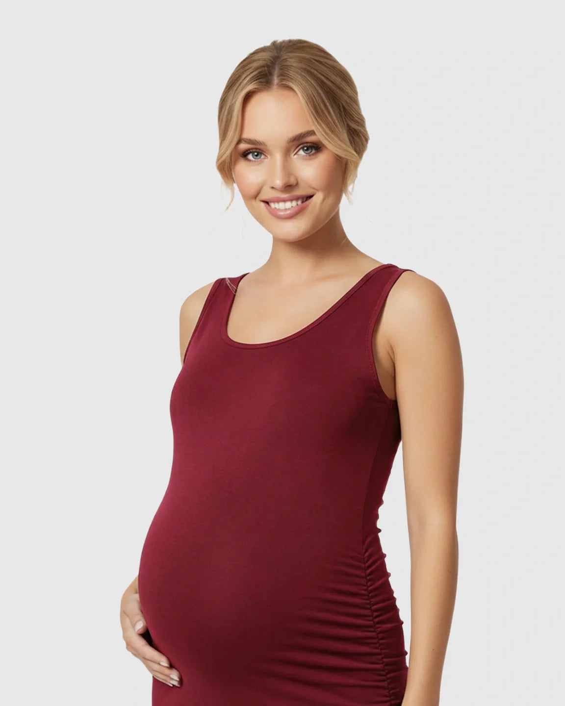 Smiling pregnant woman in a burgundy sleeveless camisole bodycon maternity dress with side pleats.