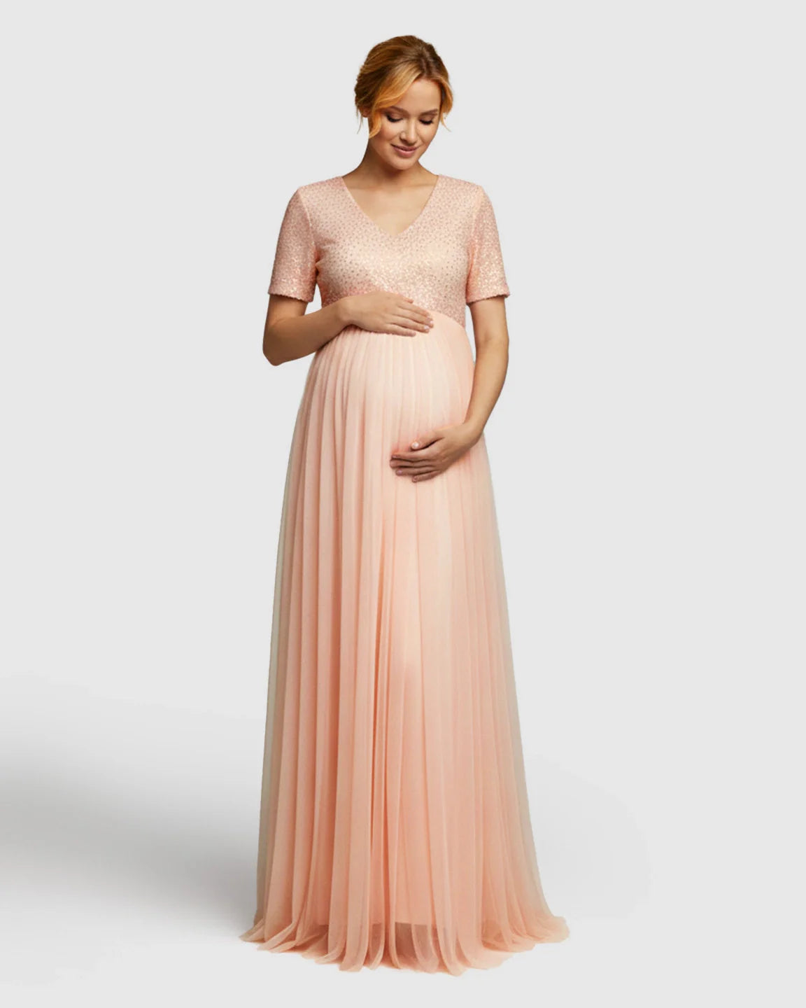 Pregnant woman in a pink sequin A-line maternity evening gown with a flowing mesh skirt.