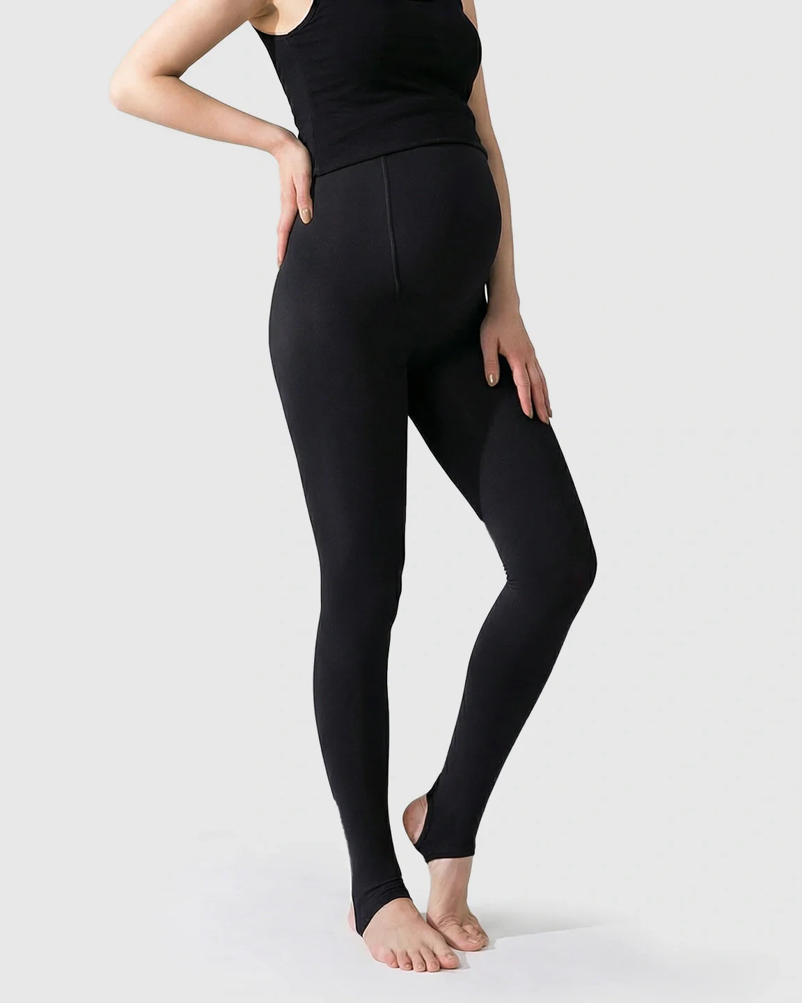 Black fleece-lined over-bump maternity leggings with stirrup design, modeled on a pregnant woman.