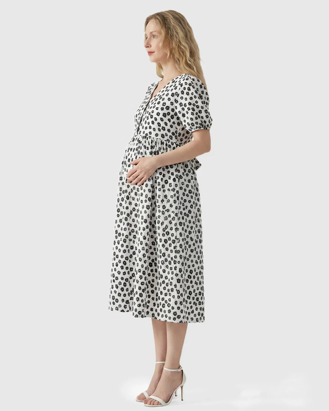 Woman in white floral print midi maternity nursing dress with V-neck and button-front, holding belly.
