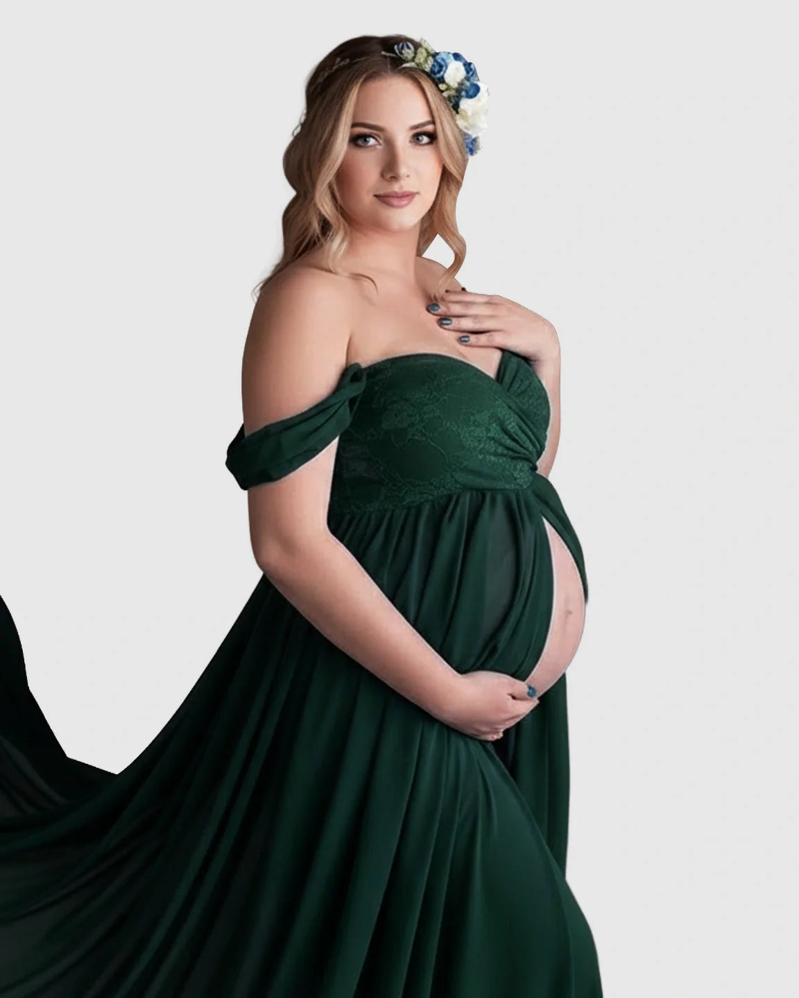 Pregnant woman in an emerald green off-shoulder chiffon maternity gown with a long train and floral headband.