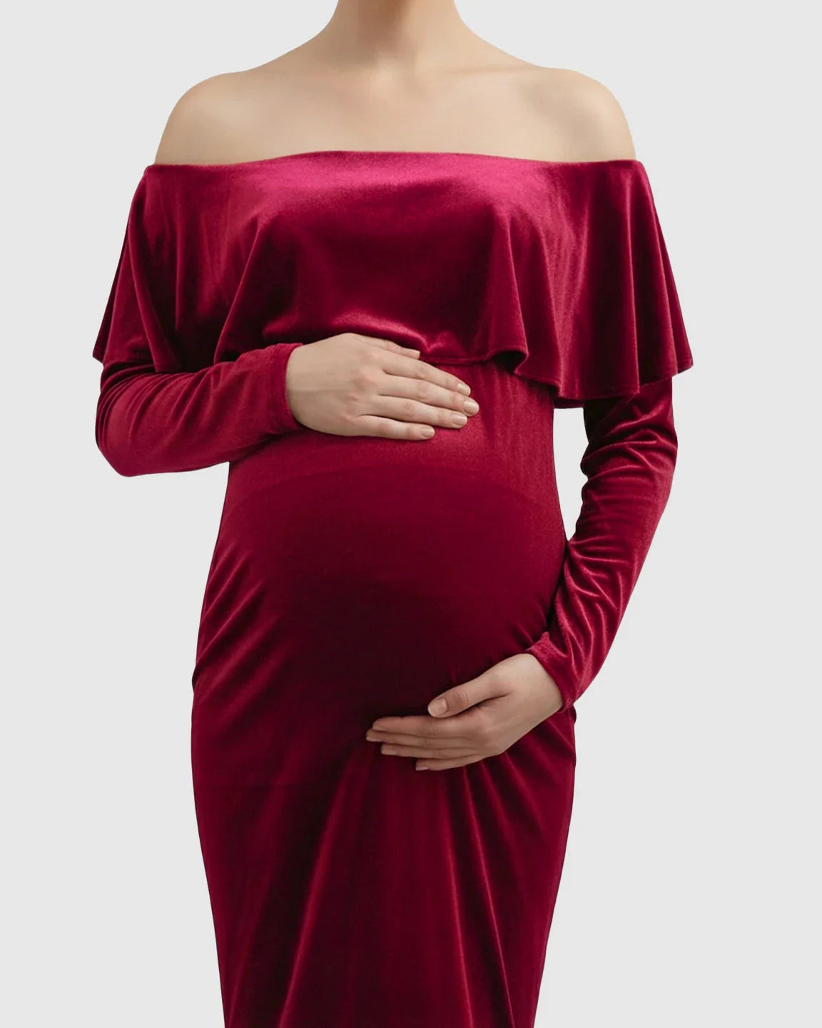 Red velvet off-shoulder maternity gown with a ruffled bodice, long sleeves, and a fitted silhouette.