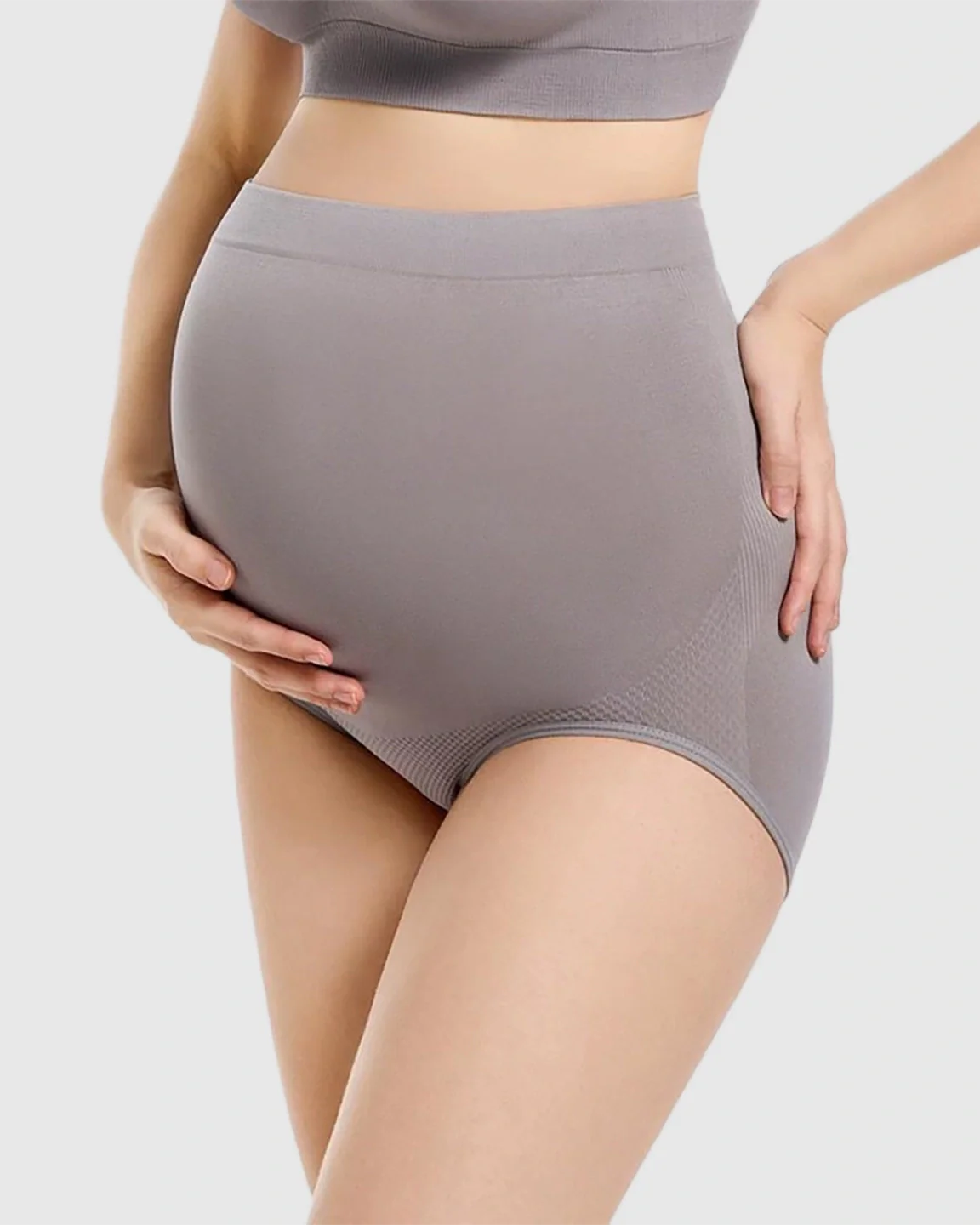 Pregnant woman wearing gray seamless high-waist maternity panties, supporting her bump.