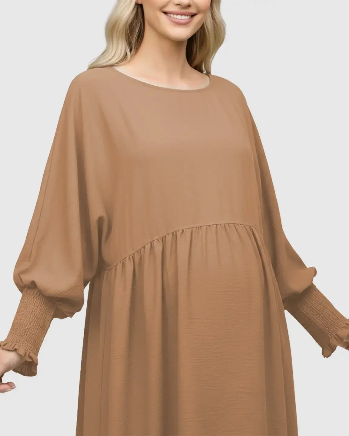Smiling woman in a brown smocked-sleeve maternity dress with a round neckline and flowing silhouette.