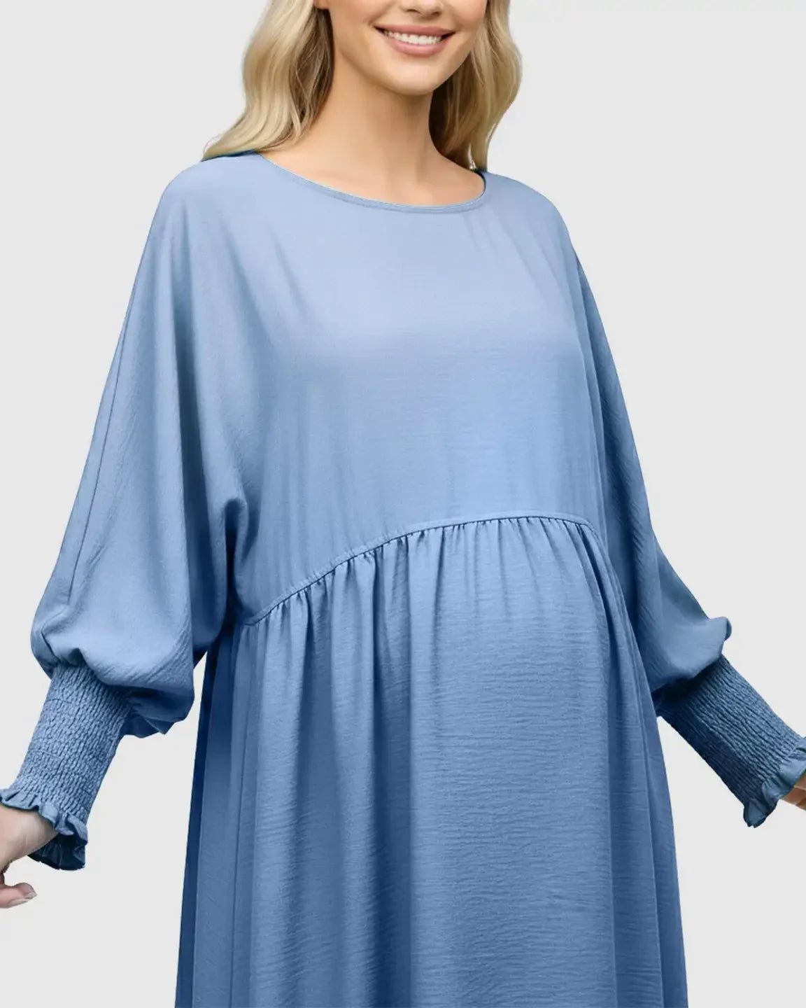 Smiling pregnant woman in a light blue smocked sleeve casual dress with a round neckline.