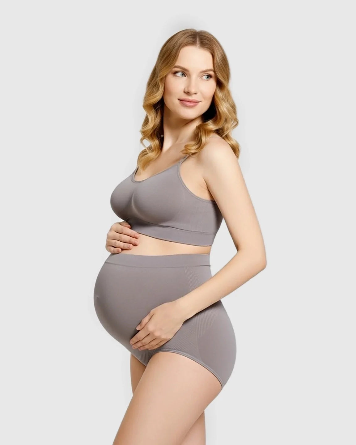 Pregnant woman in a gray seamless high-waist maternity panty and matching bra, supporting her bump.