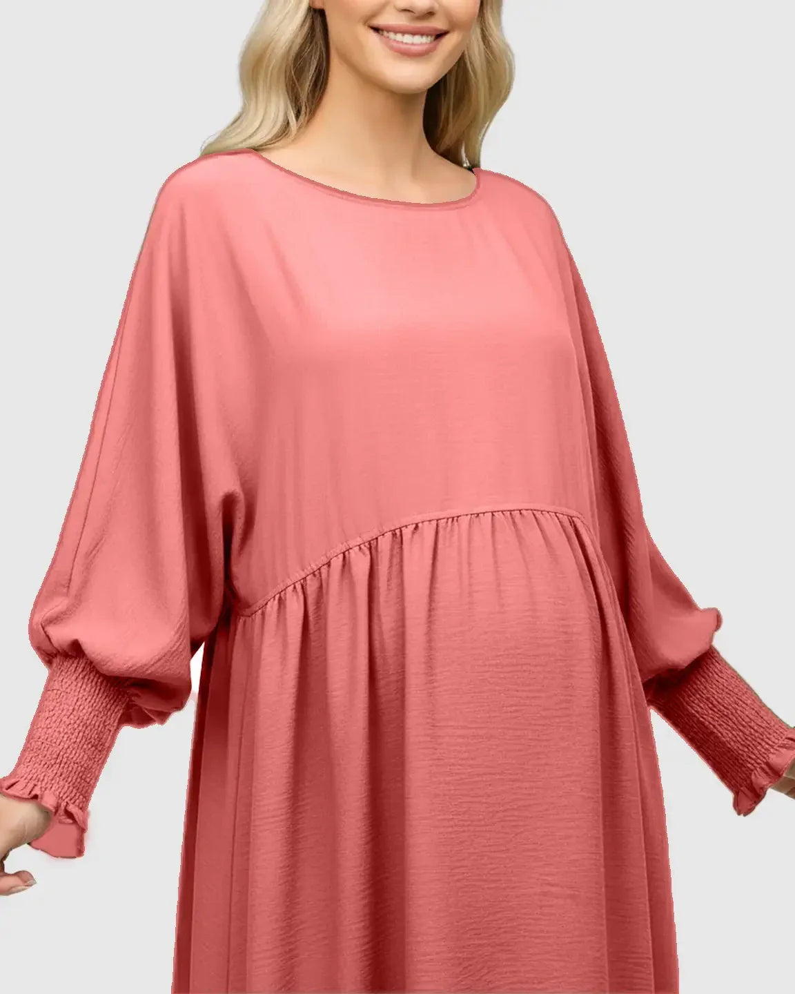 Smiling pregnant woman in a coral pink smocked sleeve casual dress with a round neckline.