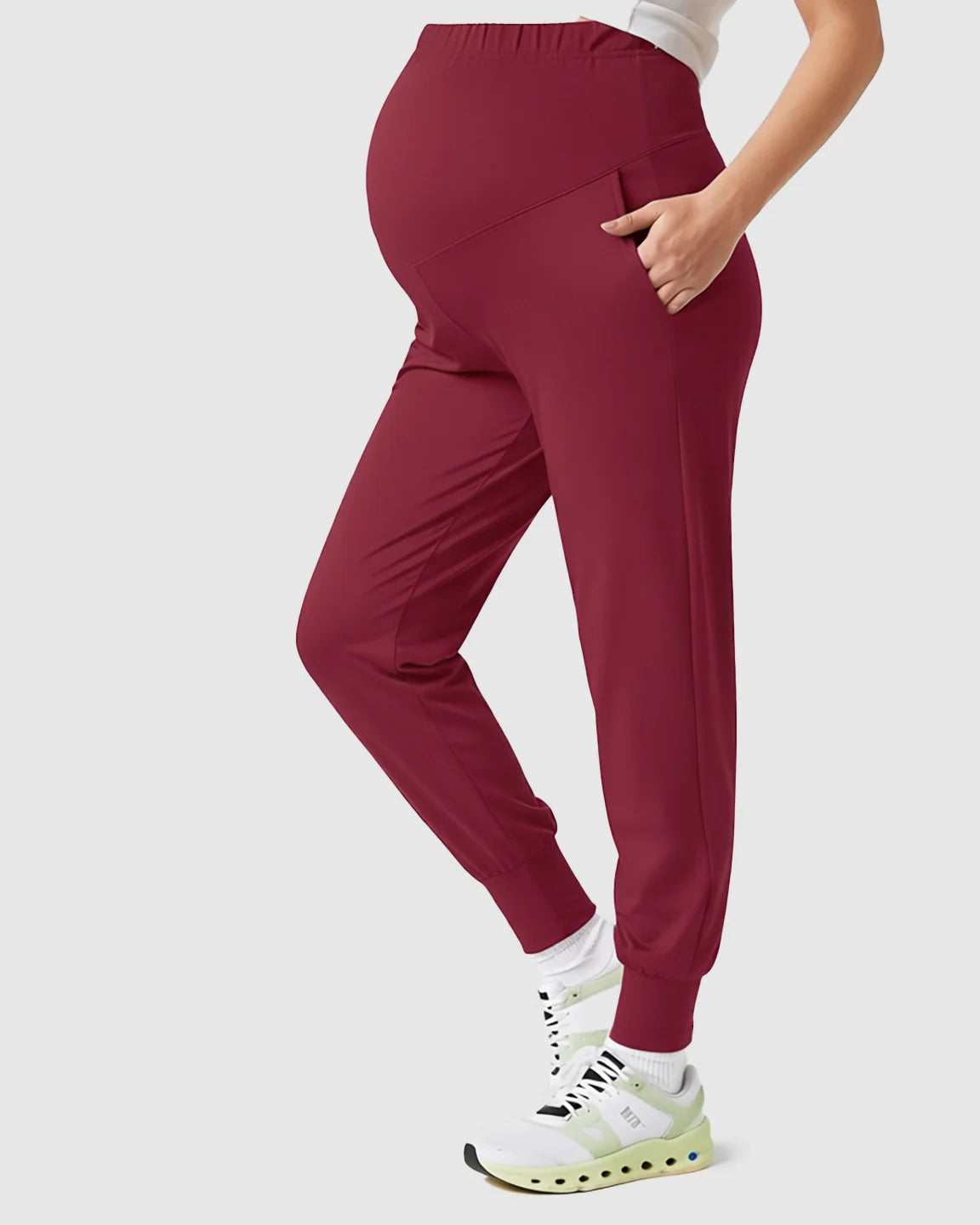 Maternity joggers in supportive, slim-fitting burgundy with a high-waist and pockets, worn by a pregnant model.