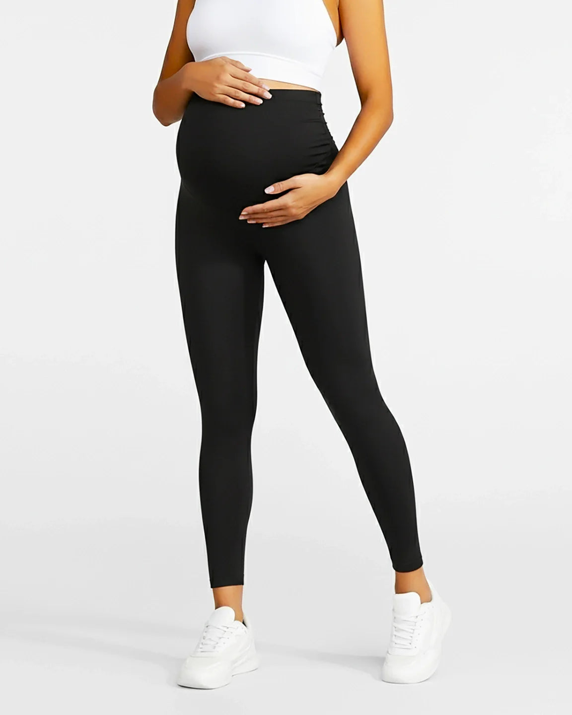 Woman in black sculpting ankle-length maternity leggings with an over-the-bump waistband, paired with a white top.