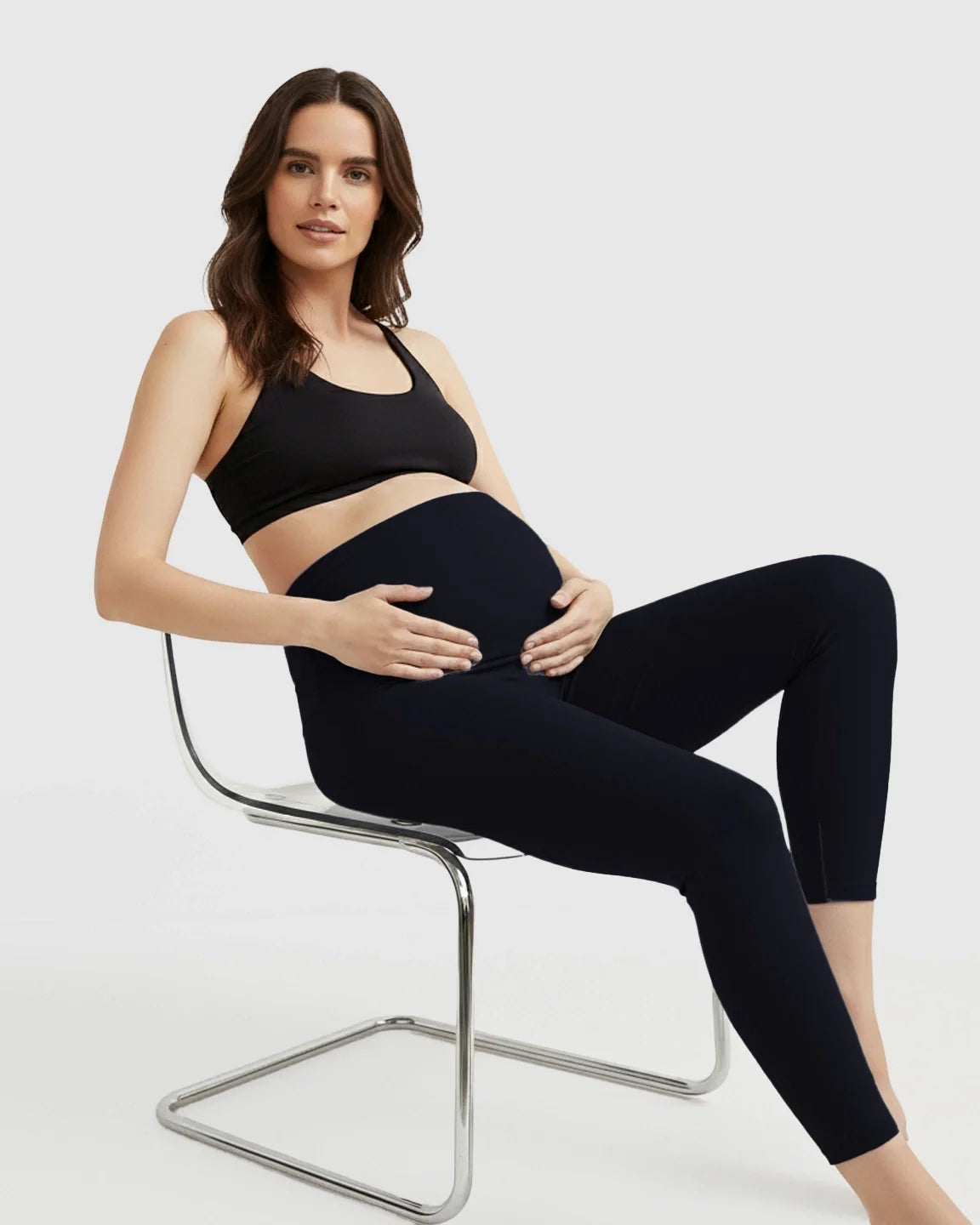 Pregnant woman in black Bump Society ultra-soft support maternity midi leggings and bra, cradling her bump.